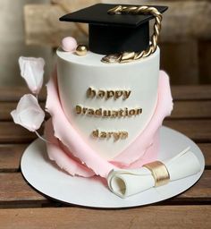 a graduation cake is decorated with pink and white frosting, gold lettering and a black cap on top