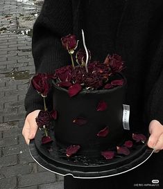 a person holding a black cake with red flowers on it