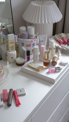 a white vanity topped with lots of cosmetics and personal care items next to a mirror