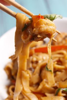 chopsticks holding up noodles with vegetables and sauce in a white bowl on a blue table