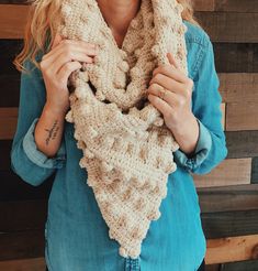 a woman wearing a knitted scarf in front of a wooden wall