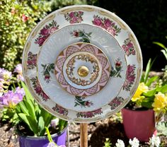 there is a plate that has been placed on a stand in front of flowers and potted plants