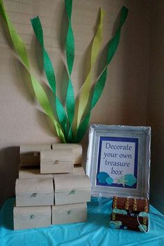 a table topped with boxes and a vase filled with green leaves next to a sign