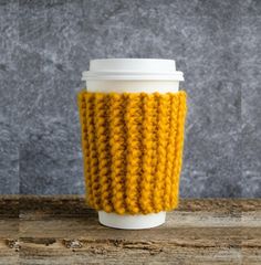 a knitted coffee cup cozying in yellow and white, sitting on a wooden table