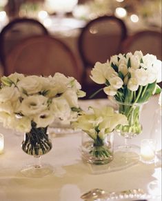 white flowers in vases on a table with silverware and candlelight holders for centerpieces