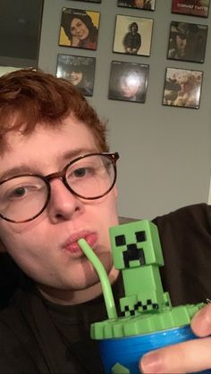 a man in glasses drinking from a cup with a creeper on it's mouth