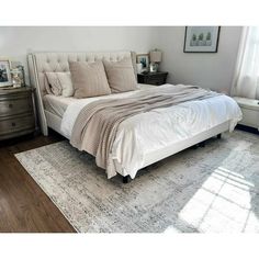 a white bed sitting on top of a wooden floor next to a dresser and window