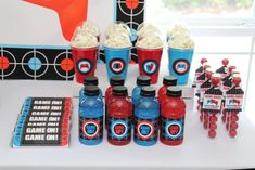 a table topped with red and blue cups filled with popcorn next to bottles of soda