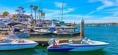 several small boats are docked in the water near a pier with palm trees and ferris wheel