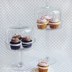 three cupcakes under a glass dome on top of a cake stand with two other cupcakes underneath it