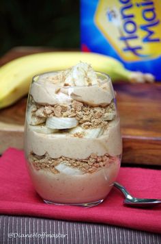 a dessert in a glass on top of a pink napkin next to a banana and yogurt container