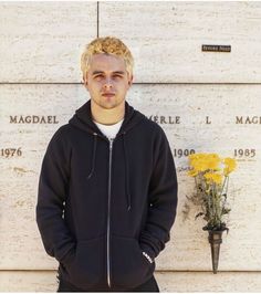 a young man standing in front of a wall with flowers and a plaque on it