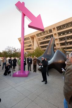 a group of people standing in front of a large pink sculpture with an arrow on it