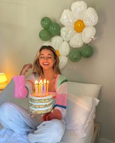 a woman sitting on a bed holding a cake with lit candles in front of her