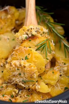 a wooden spoon is in a slow cooker filled with potatoes and meat, topped with parmesan cheese