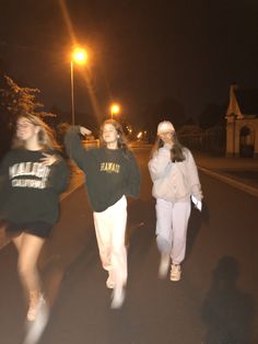 three girls are walking down the street at night, one is holding her arm up