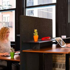 two women sitting at desks in an office setting, one using a laptop and the other working on her computer