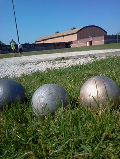 three metal balls sitting in the grass next to each other on a field near a building