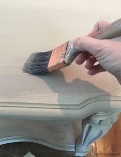 a person holding a paintbrush over a white painted piece of furniture that has been stripped off