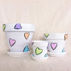 three pots with hearts painted on them sitting in front of a white background and one has two cups next to it