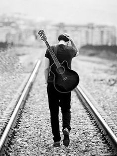 a man walking down train tracks holding a guitar