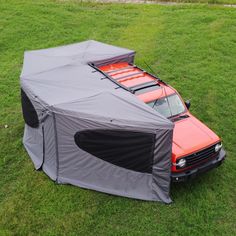 an orange truck parked in the grass with a cover on it's hood and roof