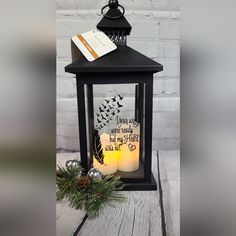 a black lantern with two lit candles and a note attached to the candle is sitting on a wooden table