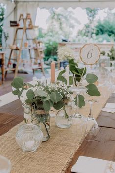 the table is set up with wine glasses and greenery in vases on it