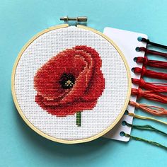 a cross - stitch red flower on a white background next to some tassels