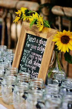 there is a sign on the table with mason jars and sunflowers in it