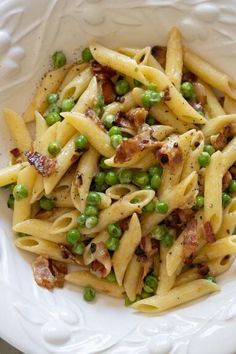 a pasta dish with peas and bacon in a white bowl on top of a table