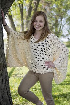 a woman standing next to a tree wearing a crocheted shawl and smiling