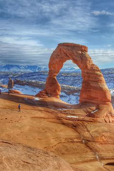 a large rock formation in the middle of a desert with snow on it and people walking around