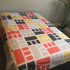 a bed covered in a colorful quilt next to a potted plant