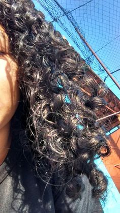 a woman with long curly hair standing in front of a fence and looking up at the sky