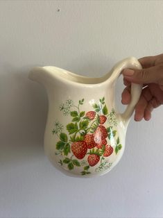 a hand holding a white pitcher with strawberries painted on it