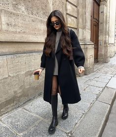 a woman in black coat and boots walking down the street