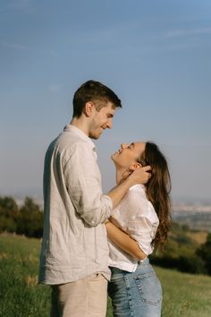 a man and woman are standing in the grass looking into each other's eyes