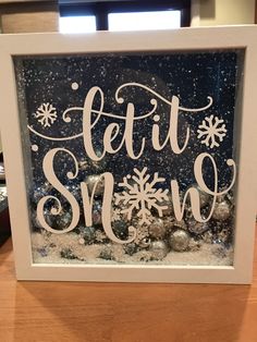 a white framed sign that says let it snow on top of some snowflakes