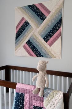 a teddy bear sitting on top of a crib next to a quilted wall hanging