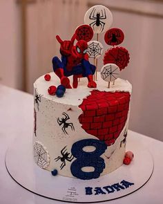 a spiderman themed birthday cake on a white table with red, blue and black decorations