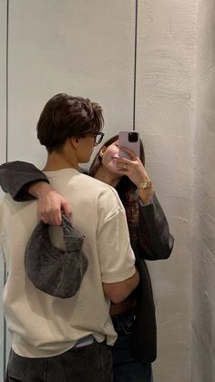 a man and woman standing in front of a mirror looking at their cell phones together