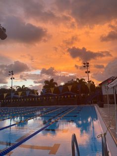 an empty swimming pool with the sun setting in the background and clouds reflecting on the water