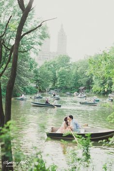 a man and woman kissing in a boat on a river with boats floating down it