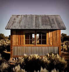 a small wooden building with a metal roof and window on the side in an open field