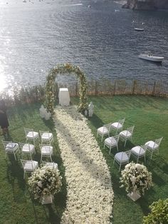 an outdoor ceremony setup with white flowers and greenery on the grass by the water