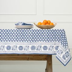 a blue and white table cloth with oranges in a bowl on the side next to it