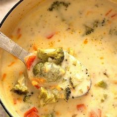 a bowl of soup with broccoli and carrots on the side next to a spoon