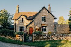 a stone house with red door and windows on the side of a road in front of some trees