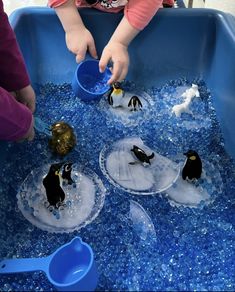 two children are playing with penguins in an ice tray